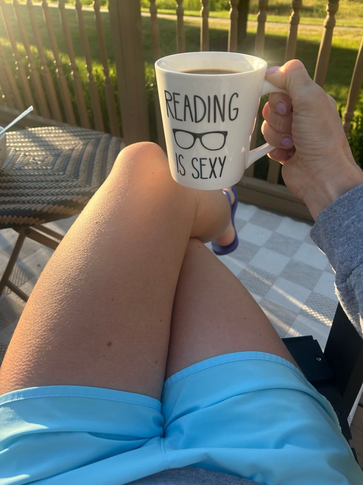 A mug of coffee. The mug has the slogan “reading is sexy” on it.  