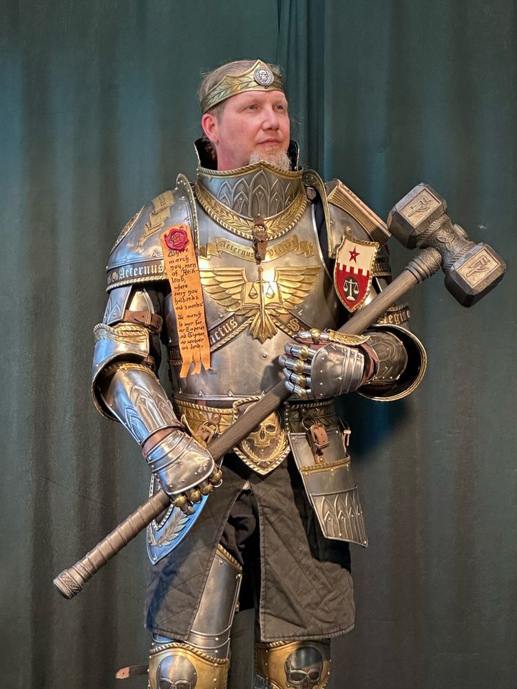 A Knight in armor holding a hammer in both arms. Steel with gold ornaments, slightly warhammer themed.