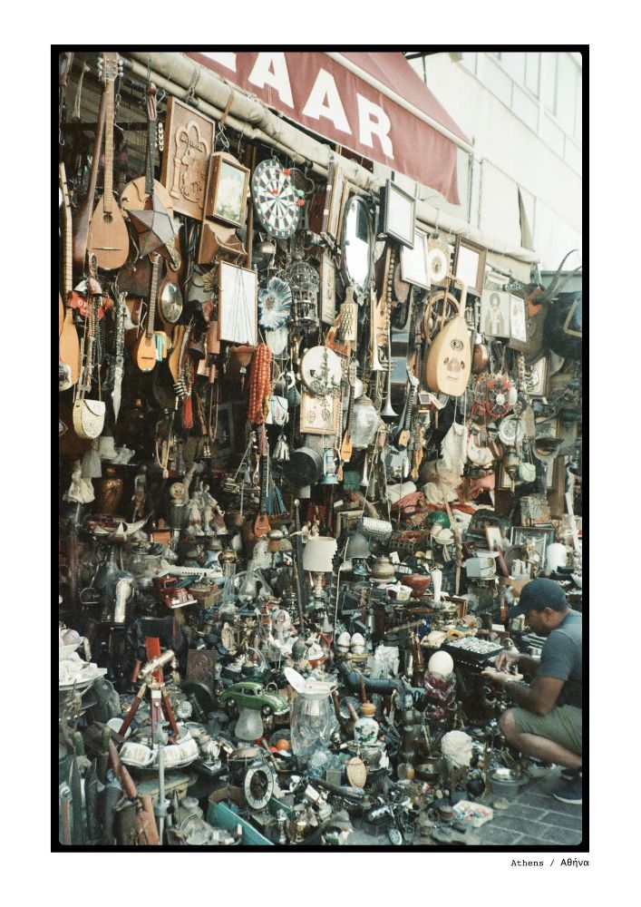 Analog picture of a big bazaar in Athens, Greece: thousands of vintage(-ish) objects hang on display in a storefront outside, with one man hunting for a treasure in the bottom right.