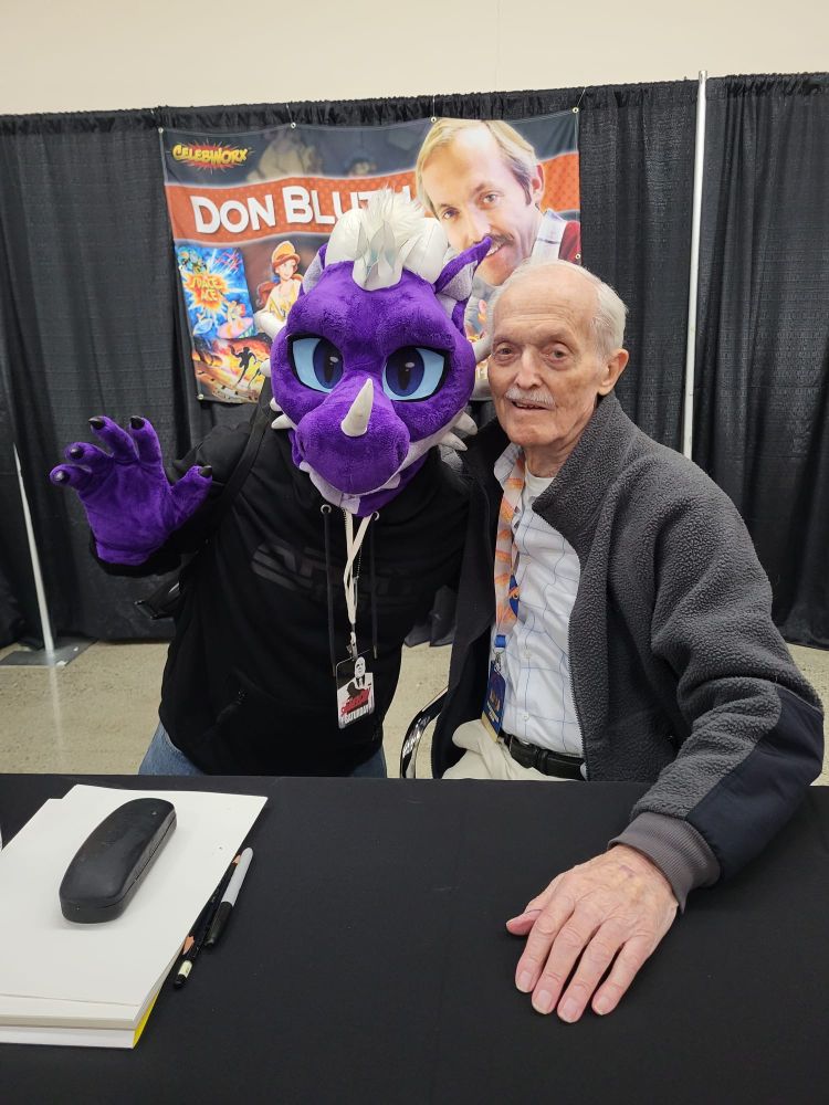 Person wearing a dragon costume waving with a legendary 2D animator