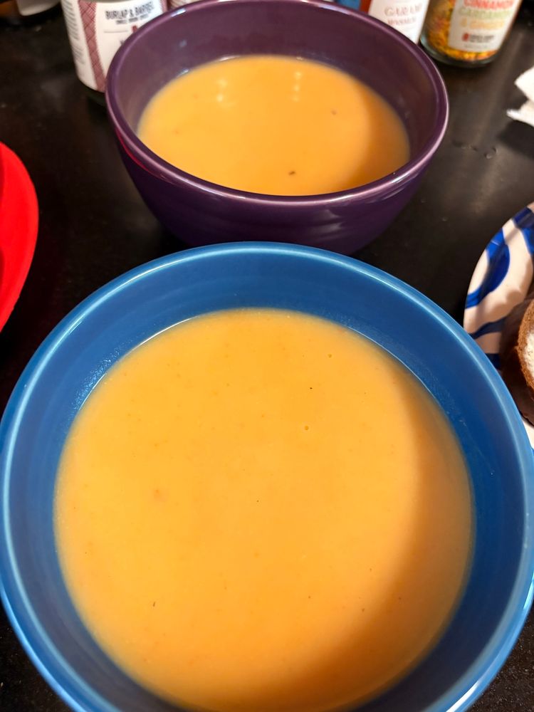 photograph of two fiestaware bowls in blue and purple, both with a yellow-orange soup in them. the soup is silky in texture. it tastes delicious. 