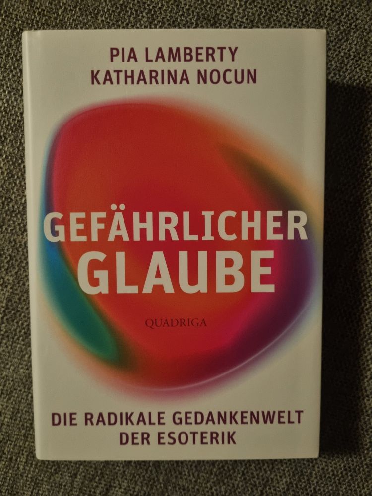 "Gefährlicher Glaube - Die radikale Gedankenwelt der Esoterik" by Pia Lamberty and Katharina Nocun. On top of a white background is a roughly oval shaped form, mainly red, with green, yellow and purple at its sides.