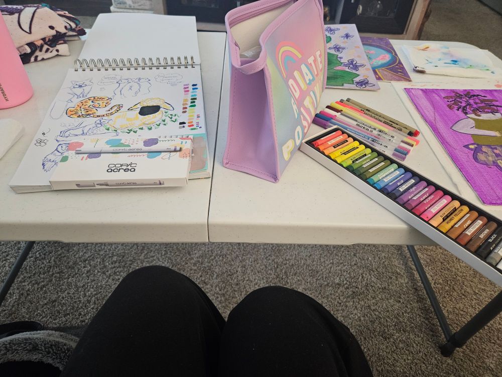 White table filled with sketchbook, pencil case, art supplies, and canvases. 