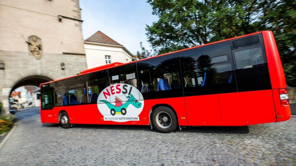 Ein roter Linienbus mit der Aufschrift NESSI, und einem darunter gemalten Drachen mit Rädern statt Beinen.