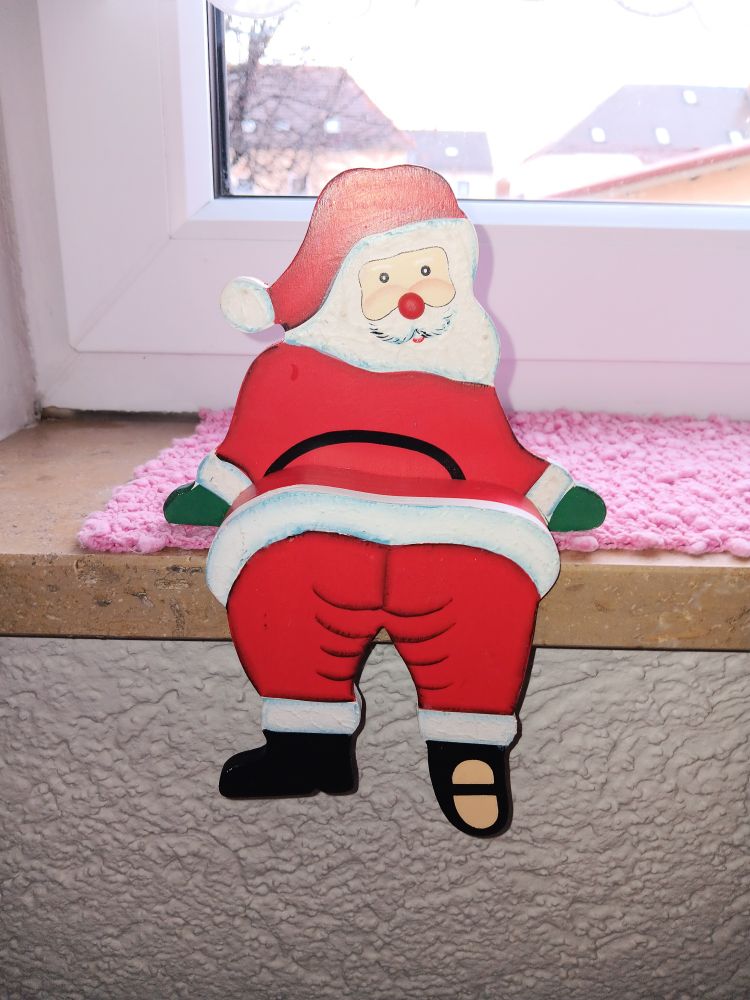 Deko-Holzfigur eines Weihnachtsmann, der aussieht, als würde er nut dem Hibtern zur Kamera ein Fensterbrett hochklettern ubd zurückschauen, wodurch es aussieht, als würde er seinen Hintern präsentieren.