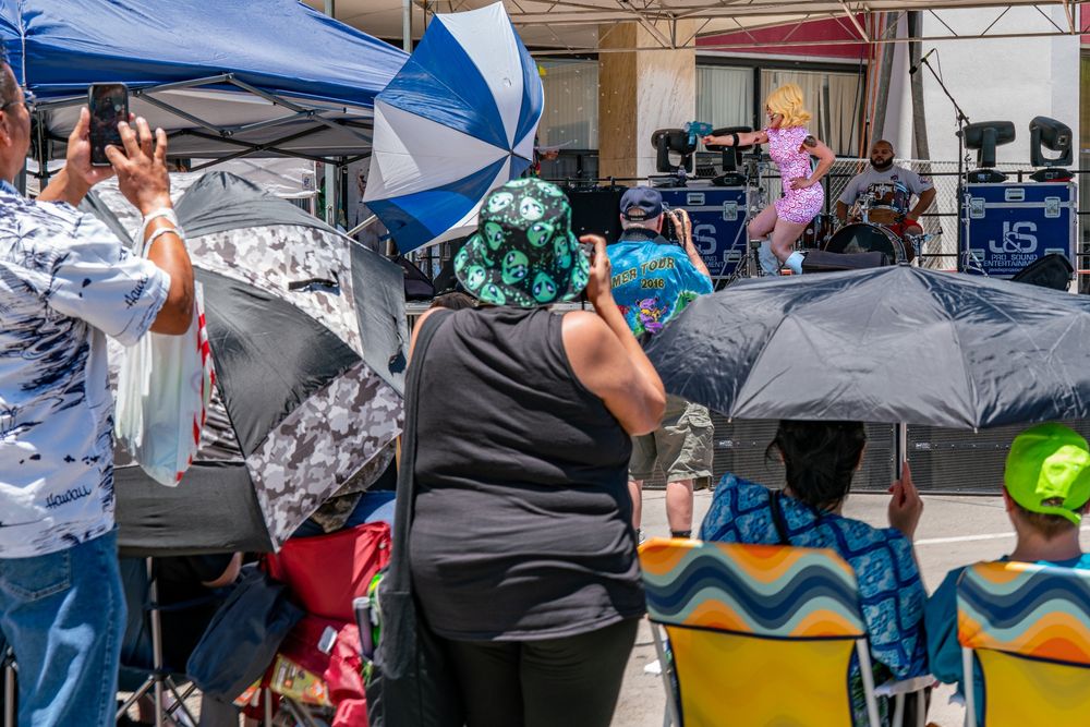 A photograph of a a women on stage dressed like the Alien women from Mars Attack. There are people and umbrellas obscuring the stage. 