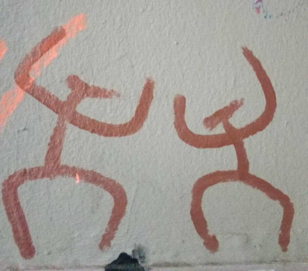 Bild zeigt Graffiti mit zwei (tanzenden?) Strichmännchen, Figuren im Stile der Höhlenmalerei.