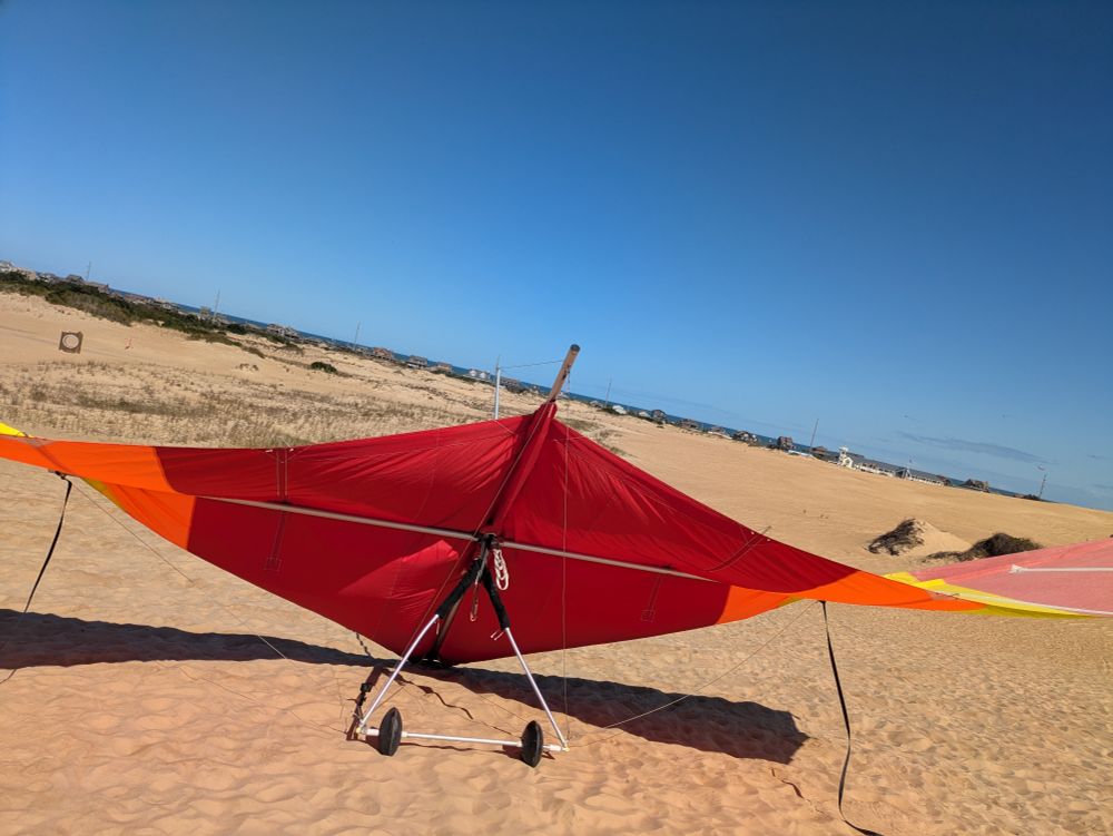 Red and yellow Hang glider perched on a dune. Blue sky above