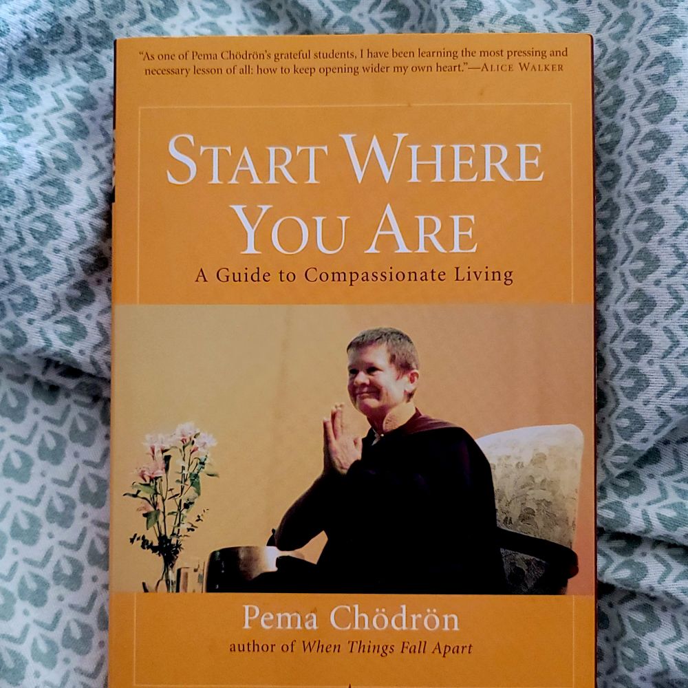This is the cover of Start Where You Are: A Guide to Compassionate Living by Pema Chodron. The cover is goldenrod yellow with a photograph of Pema Chodron with her hands together in namaste.