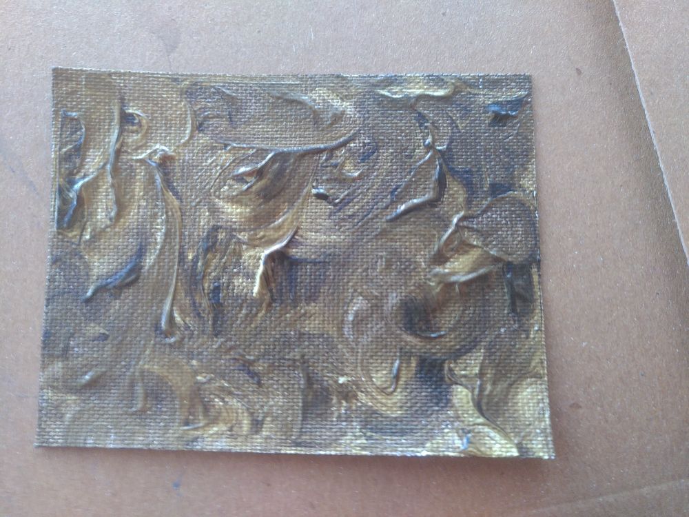 A small piece of canvas covered with swirled brown and gold paint.
