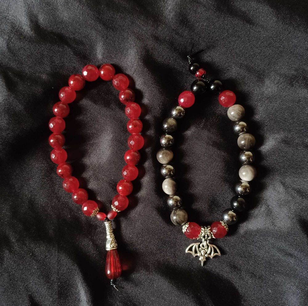 A pair of bracelets made with red and black beads with silver colored charms.