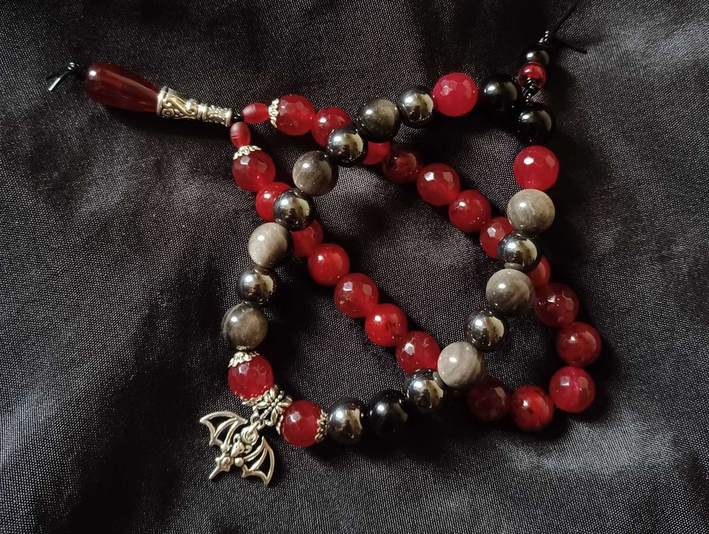 A pair of bracelets made with red and black beads with silver colored charms.