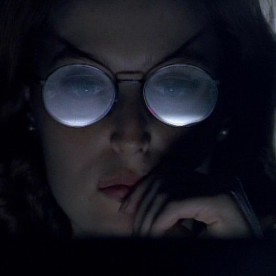Dana Scully with large round glasses looking at a screen.