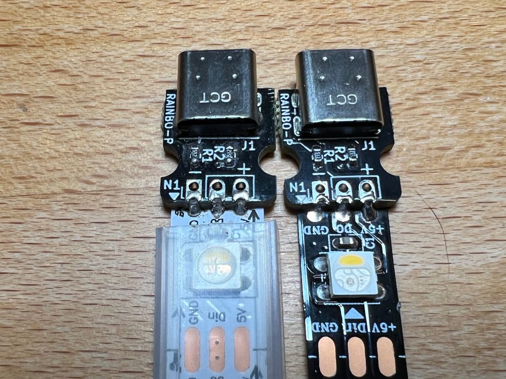 Close-up photo showing soldered castellated contacts on the circuit boards (top) connecting to their RGB strips (bottom). The solder contacts on the white strip (left), align with the contacts on its joined circuit board. The solder contacts on the black strip (right) are spaced slightly farther apart than the contacts on the circuit board as can see by the sloping shapes of the solder connections. The spacing difference is also visible in the very close contacts (bottom).