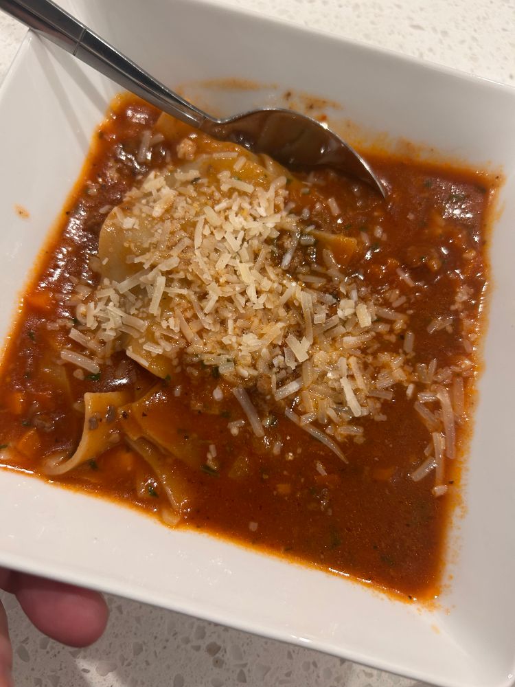 Lasagne soup in a square bowl. Meat sauce with extra beef broth and broken up lasagne noodles. Layered into the bowl with a bit of mozzarella cheese 