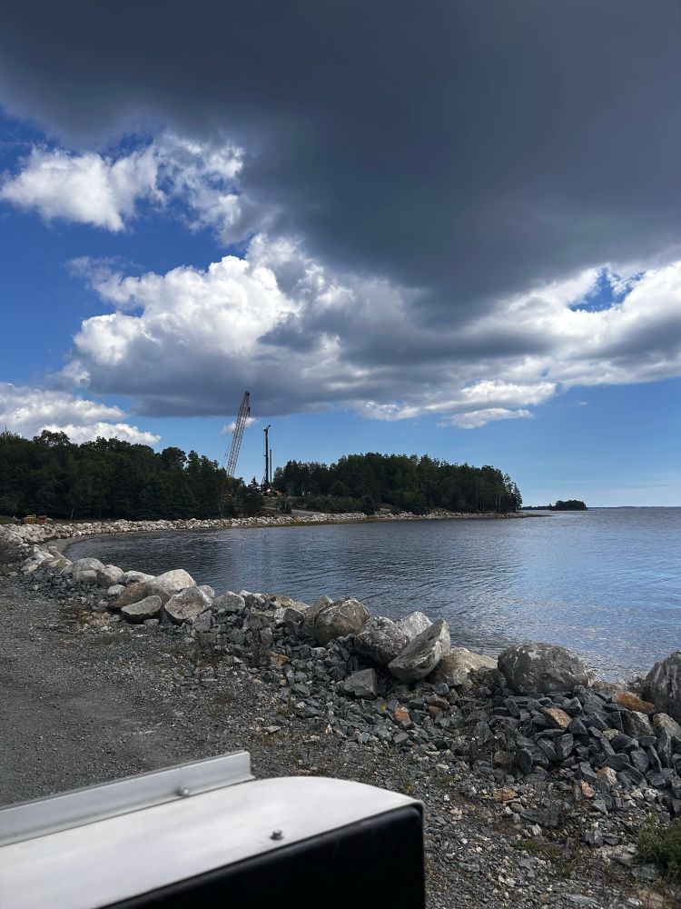A view of Smiths Cove, with a gravel shore line, trees and large cranes in the distance 