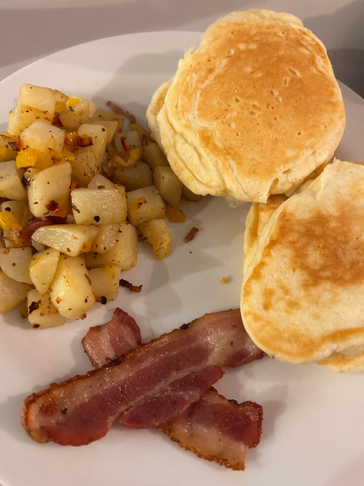 A plate with pancakes, hashbrowns and bacon 