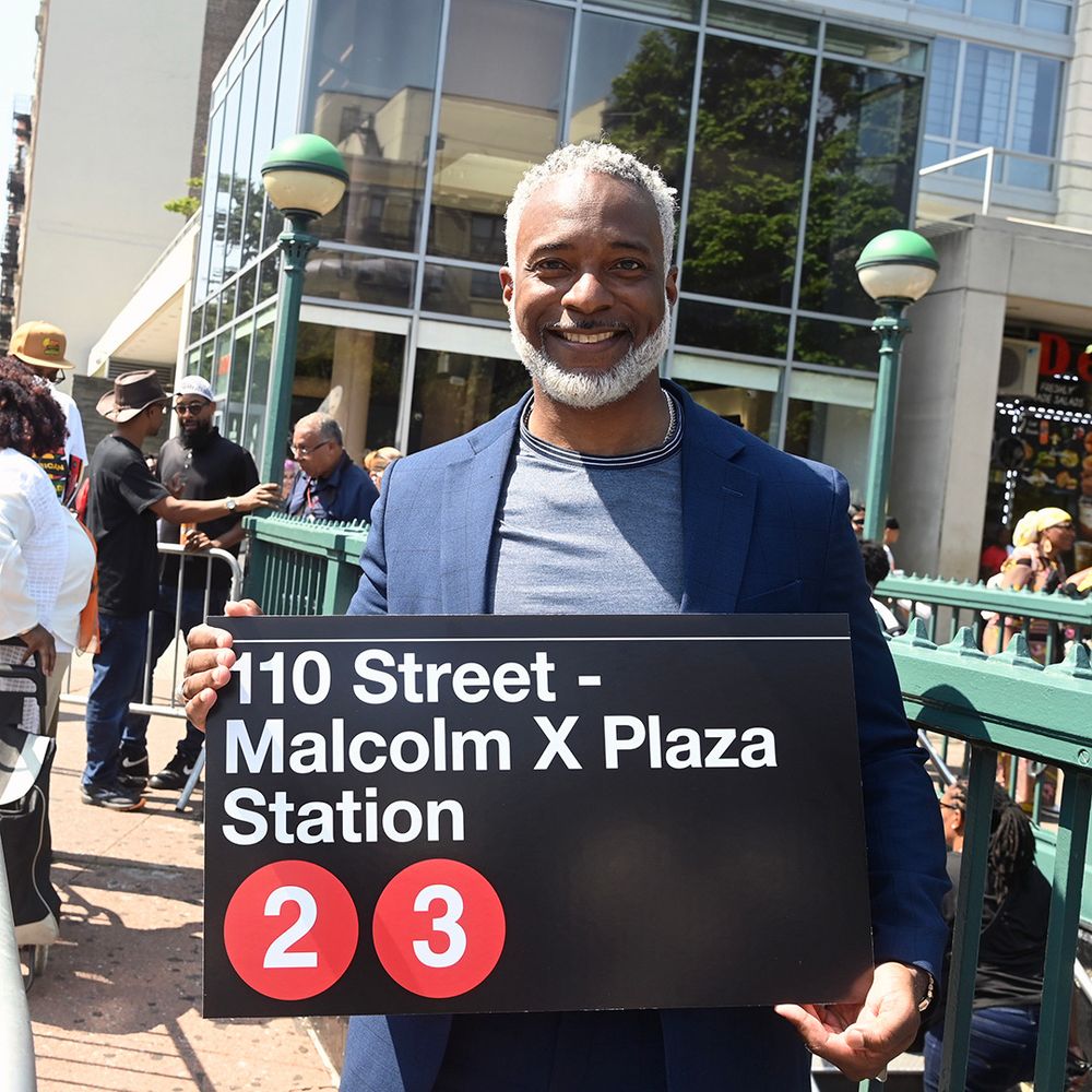NYCT President Demetrius Crichlow holding a 110 Street - Malcolm X Plaza station sign.