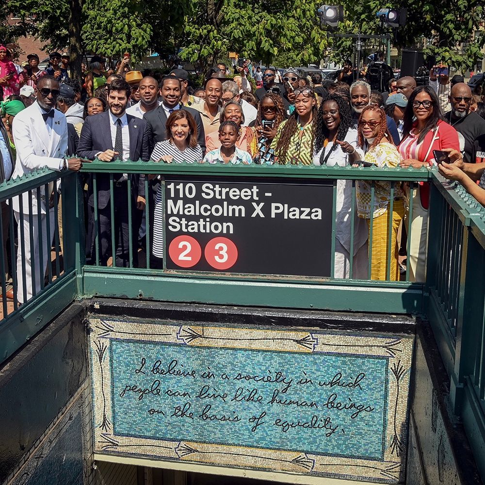 A group of people, including Governor Kathy Hochul, posing for a photo by an entrance to 110th Street - Malcolm X Plaza station.