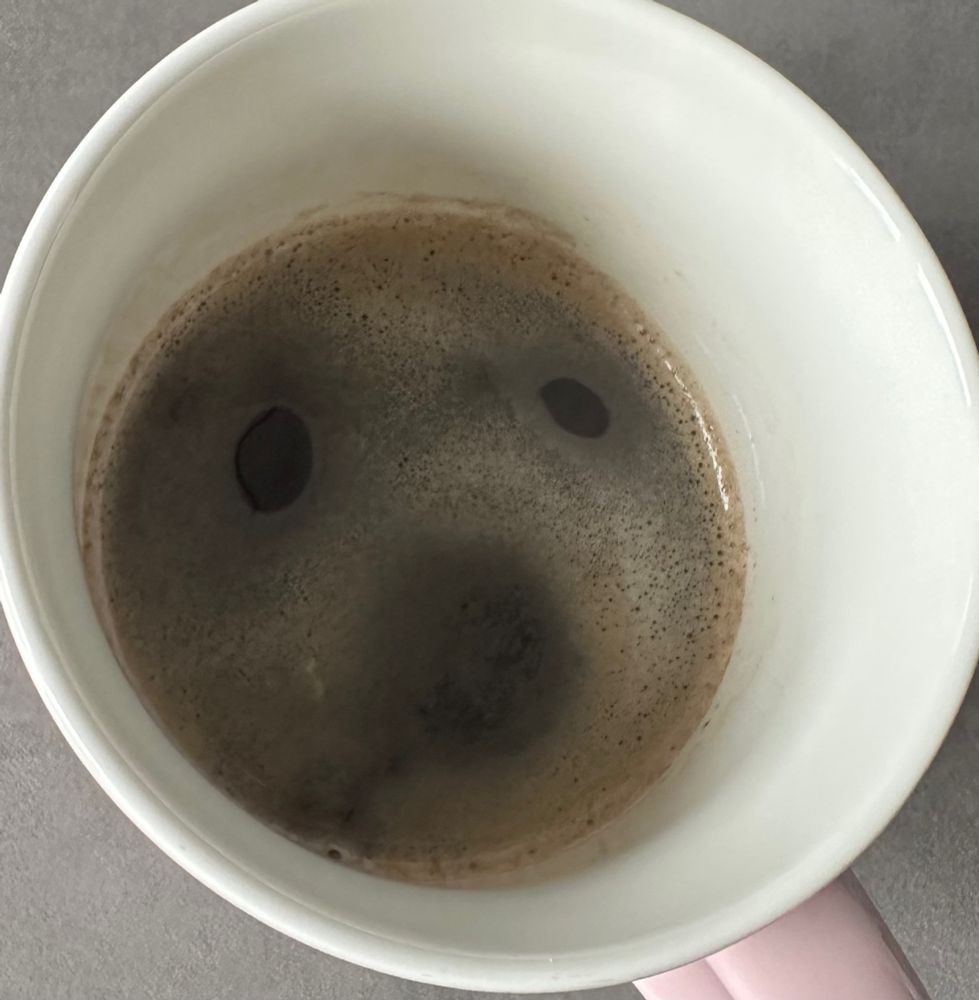 Blick in eine Kaffeetasse, wo sich in der Crema eine Art Gesicht erahnen lässt.