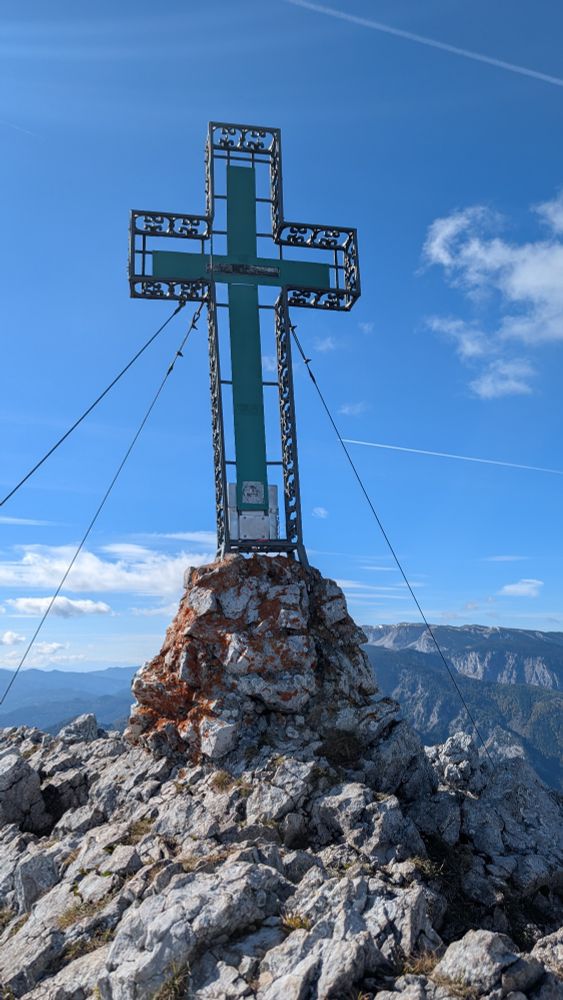 Gipfelkreuz auf Felsen, im Hintergrund Rax 
