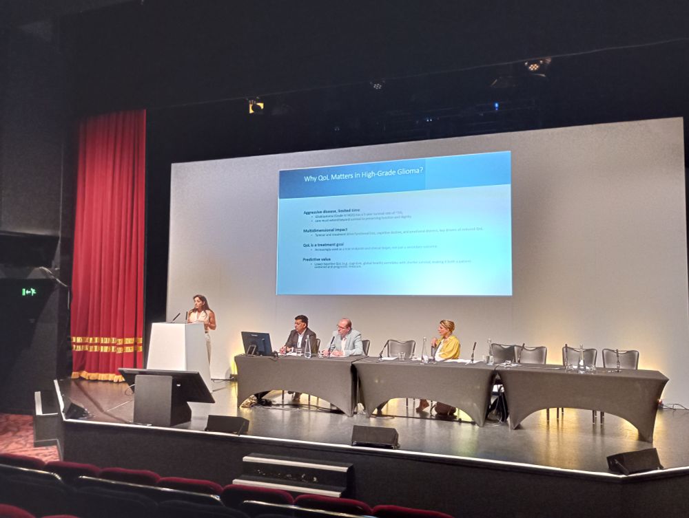 Dr. Seema Dadhania presenting on stage at the BNOS2025 conference, standing behind a podium. The session chairs sit at a table alongside