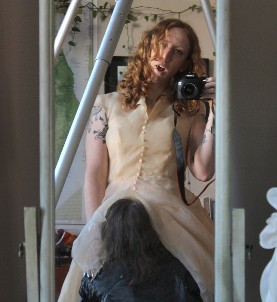 Rhiannon takes a mirror photo while her coyote sniffs hungrily under her dress.