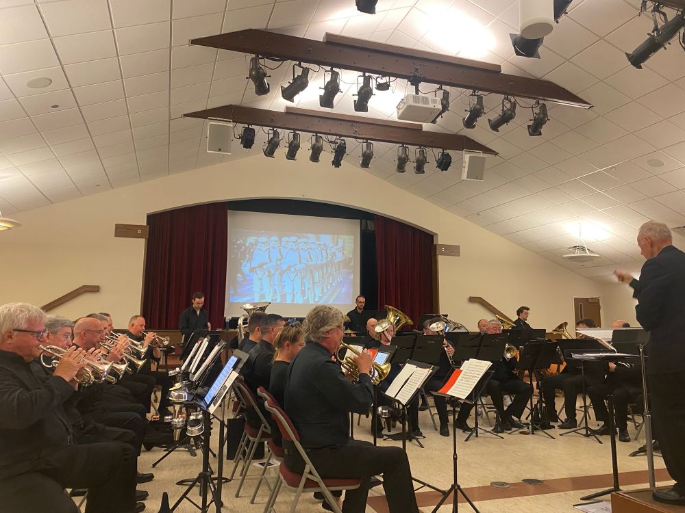 An orchestra of brass instrument musicians in a performance hall in front of a screen of Storm Troopers from Star Wars