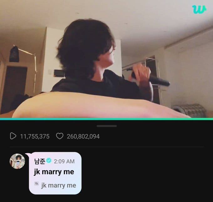 A screenshot of one of Jungkook's livestreams; He's on top, looking away towards his television, a mic loosely held in one hand. Underneath is a comment from Namjoon: "jk marry me" in English.