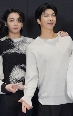 Jungkook and Namjoon cropped out of a group picture. Jungkook is wearing a soft looking black and white sweater. His hair is falling over his eyes a little and he looks kind of shy. He has one hand on Namjoon's shoulder.

Namjoon is wearing a long-sleeved white shirt that is creeping up to almost sweater paw length and is smiling at the camera. His pose happens to flatter his chest. I'm just saying.