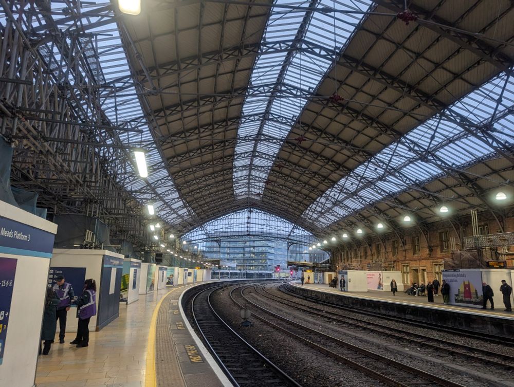A long trainshed roof with glass strips, with empty railway tracks and platforms underneath. 