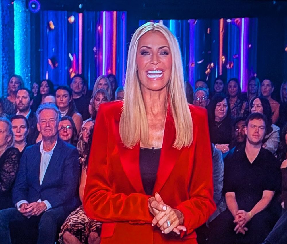 Tess Daly in a red matte jacket with red shiny lapels, smiling somewhat manically. 