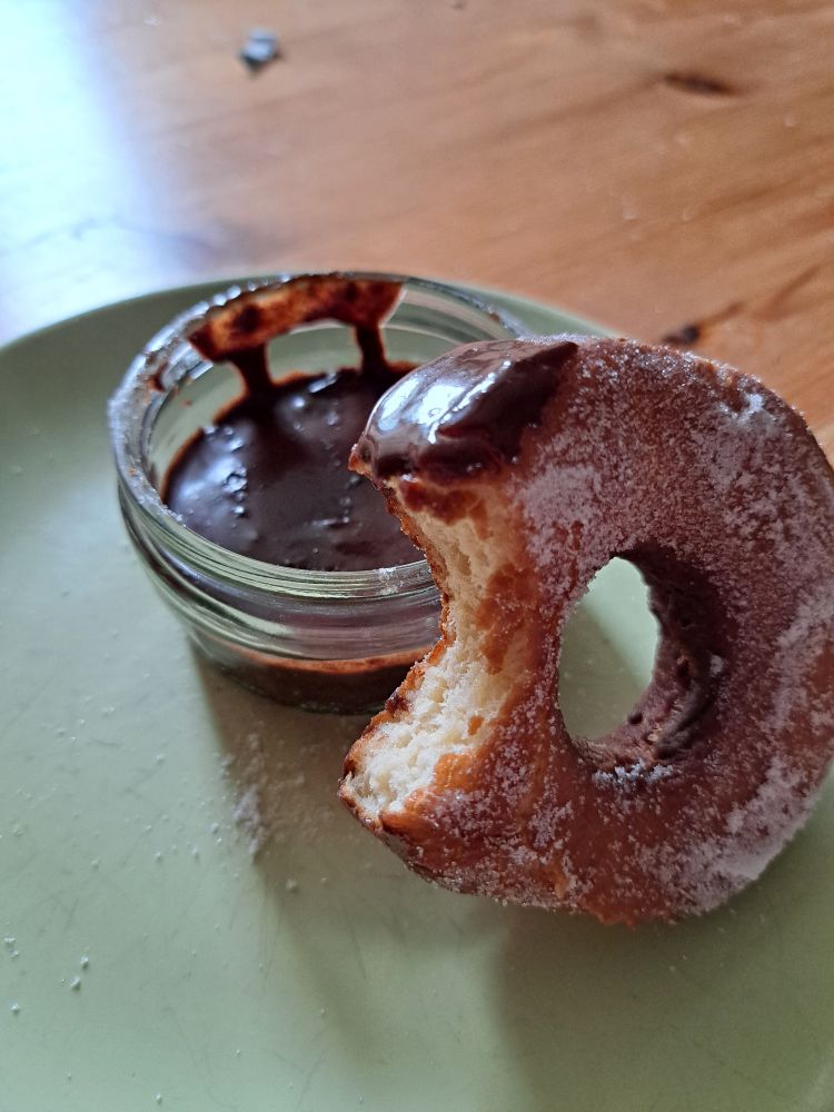 A sugar coated donut on a green plate with a bowl of chocolate sauce 