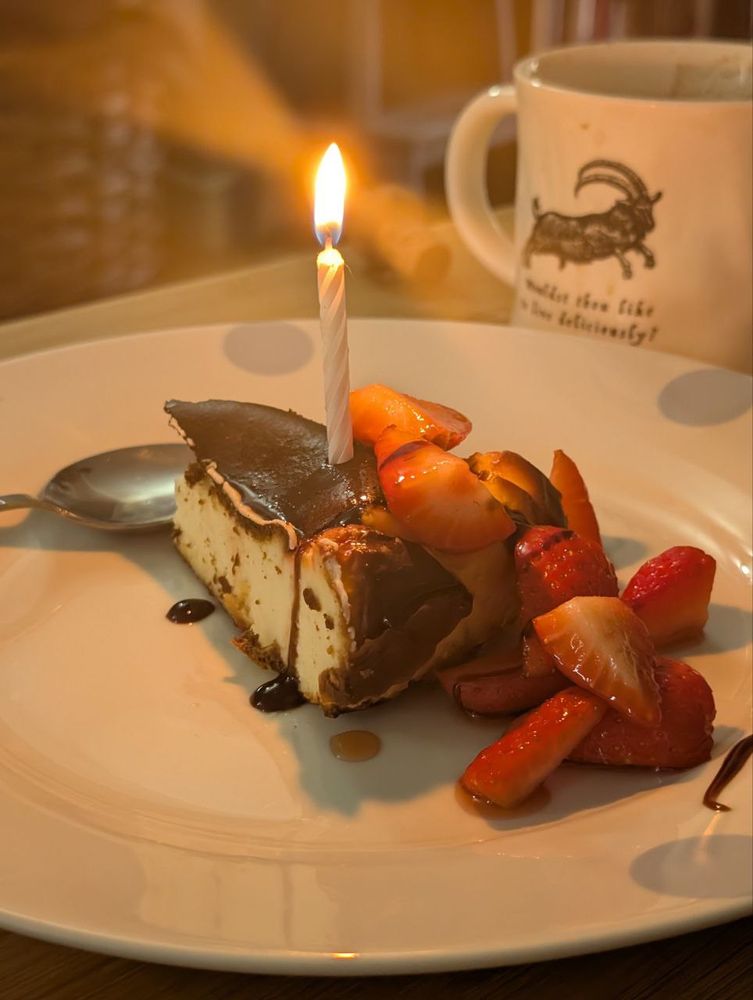 Cheese cake with strawberries and a balsamic reduction. There is a small on fire birthday candle stuck in it 
