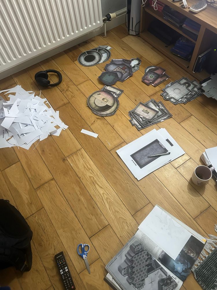 On a pale wooden floor that are piles of cut out bits of castle ravenloft .The is a very large pile of white paper scraps 