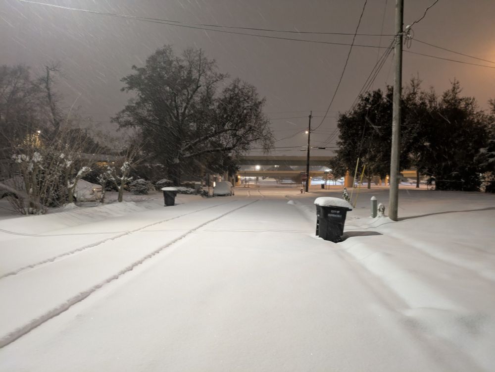 A snow-covered city street at night. Everything looks gray and white and quiet.