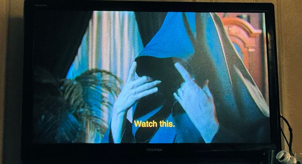 The Ghost of Christmas Yet to Cum from the show THE CHAIR COMPANY wearing her hooded cape brings her hands up to take down the hood and says “watch this”.