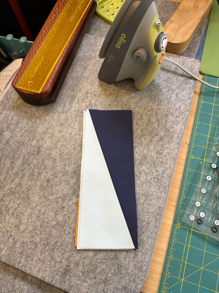 A stack of half rectangle triangles sitting on a wool pressing mat.