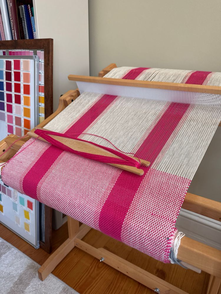 A pink and white striped warp with a dark pink weft on a rigid heddle loom.