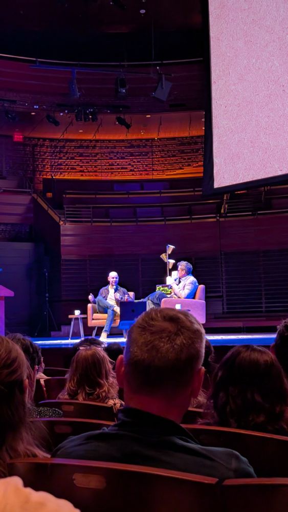 John Green and Adam Grant talking during the Philadelphia event for Everything is Tuberculosis. Some audience heads are visible. 