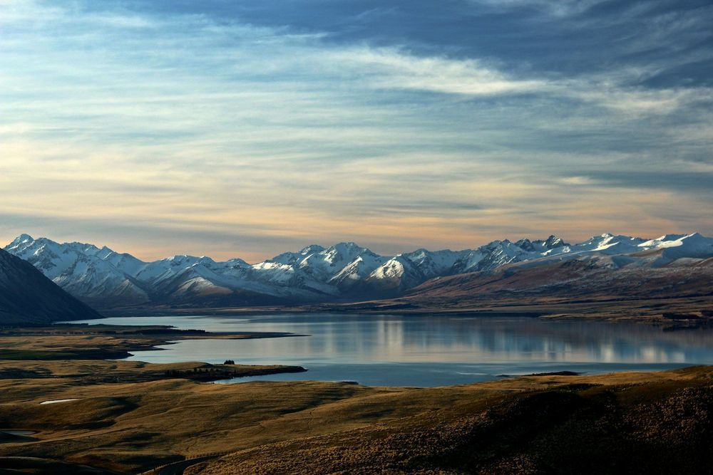 A stunning view of Lake Tekapo, New Zealand, framed by majestic mountains under a clear blue sky.