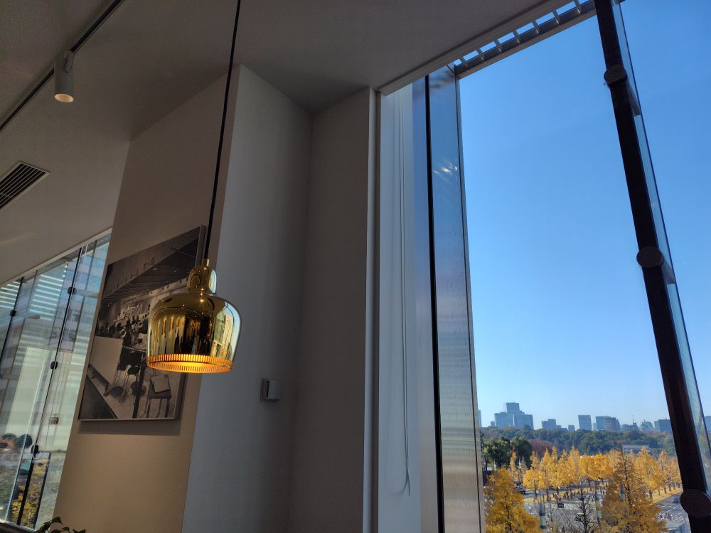 店内の様子。白壁にモノクロの写真が飾られており、その下の丸テーブルには観葉植物。右側は窓越しに見える行幸通りのイチョウ並木。