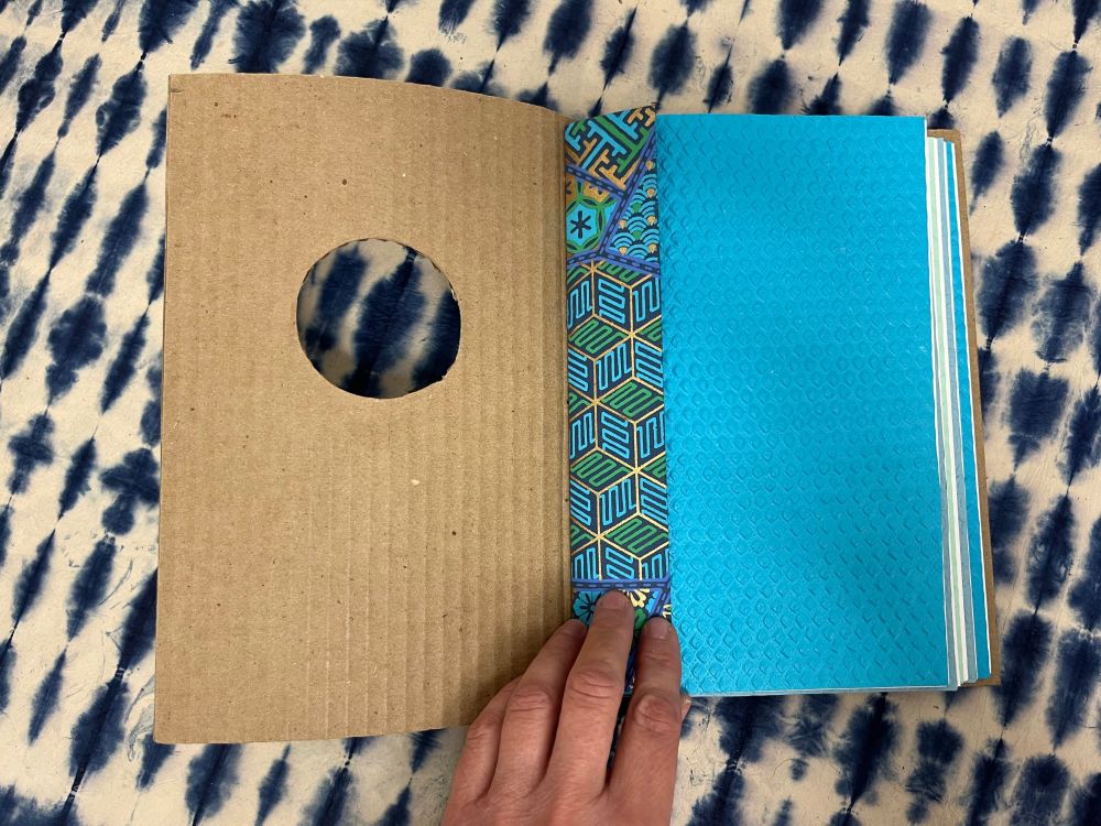 Another photograph of the book. The book is open revealing decorative and textured paper in blue.