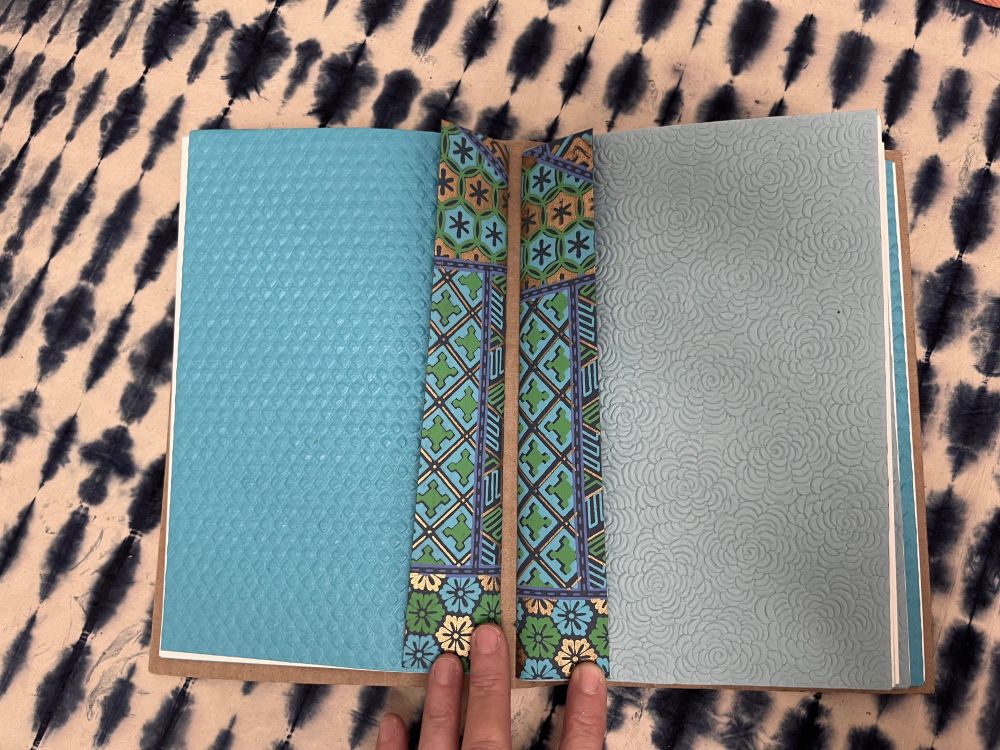 Another photograph of the book. The book is open revealing decorative and textured paper in blue and in grey.
