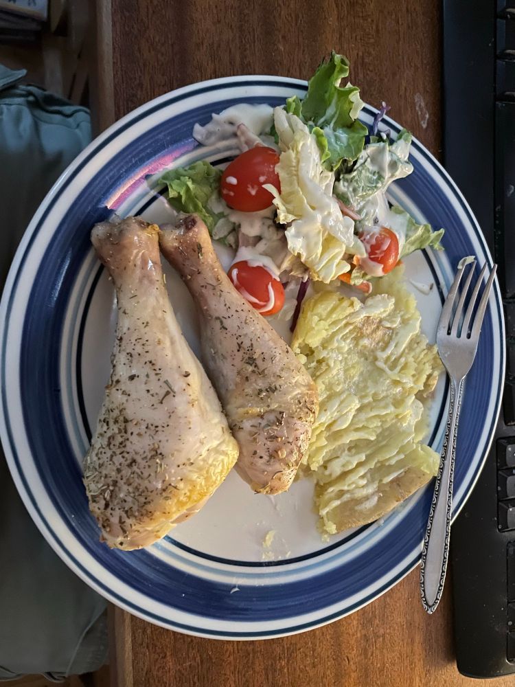 Plate of baked chicken legs, baked potato, and salad 