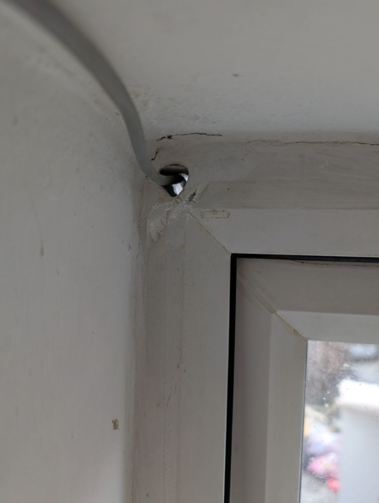 A rounded triangle hole in the corner of a window frame, with a grey wire going through it.