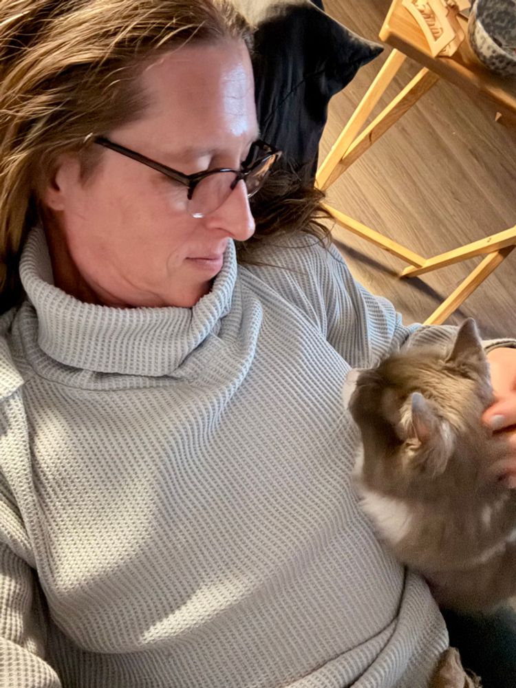Laying on the couch wearing a light blue turtleneck sweater. There’s a cat sitting beside me and we’re looking at each other while I pet her