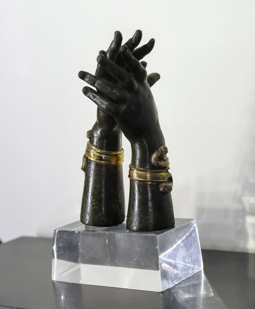 A bronze nutcracker in the shape of two hands, the fingers of which are intertwined and decorated with golden bracelets with snake heads.