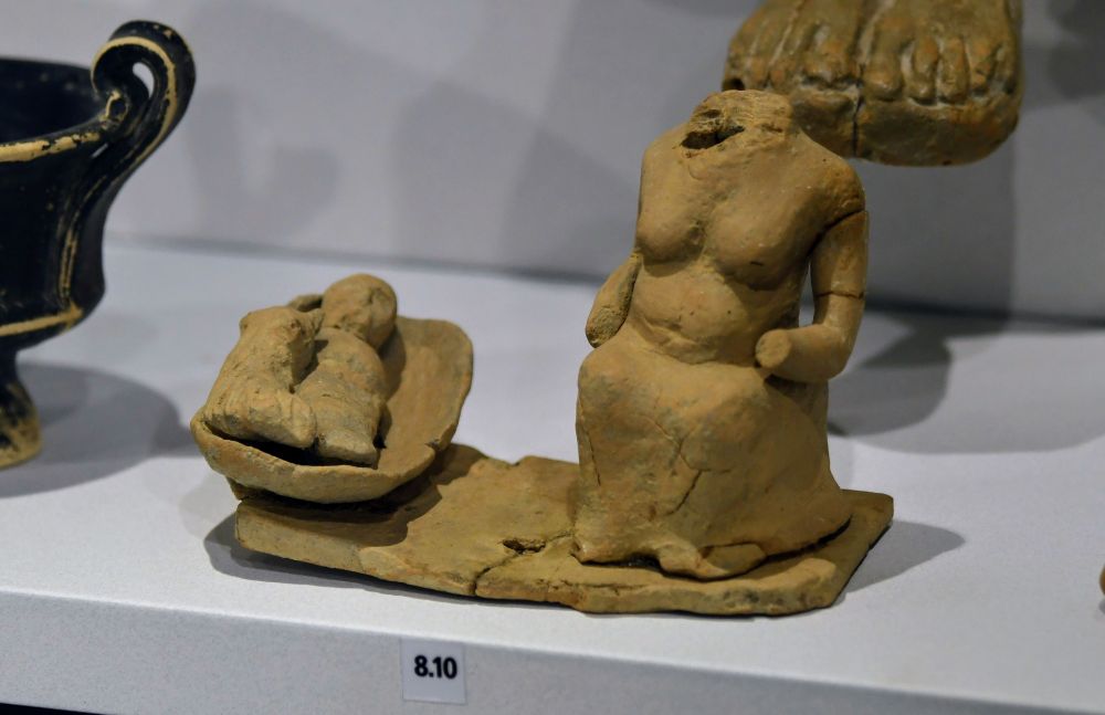 Small terracotta model of an old woman, probably a nanny, sitting next to a cradle in which a baby and a dog are sleeping.