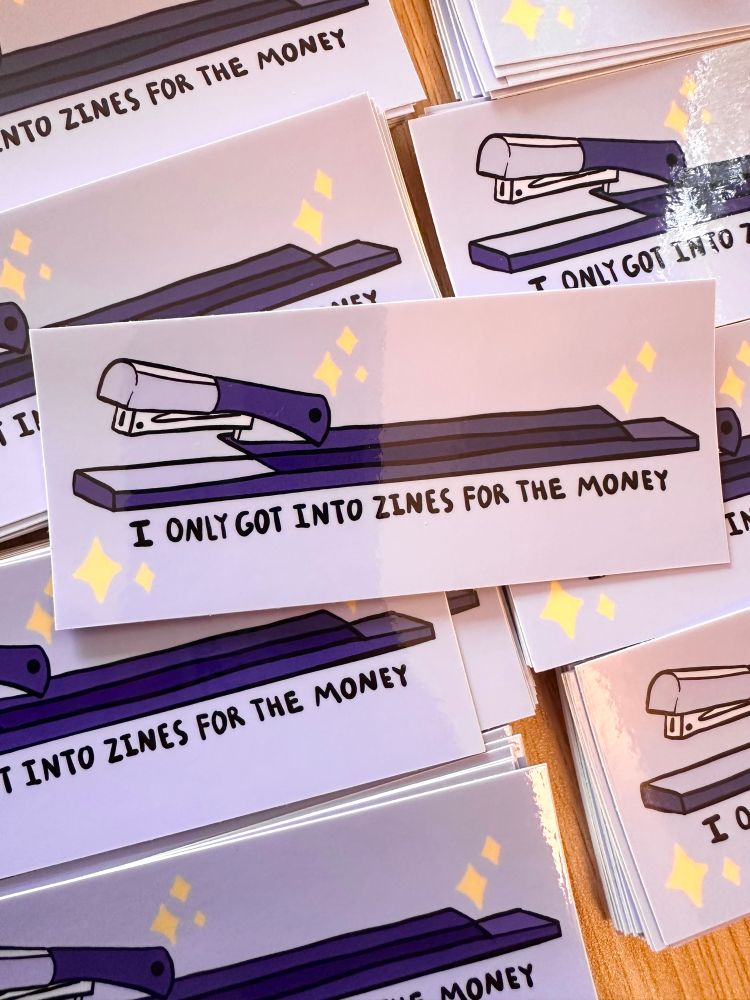 a bunch of stickers with a drawing of a long arm stapler that says “I only got into zines for the money”.